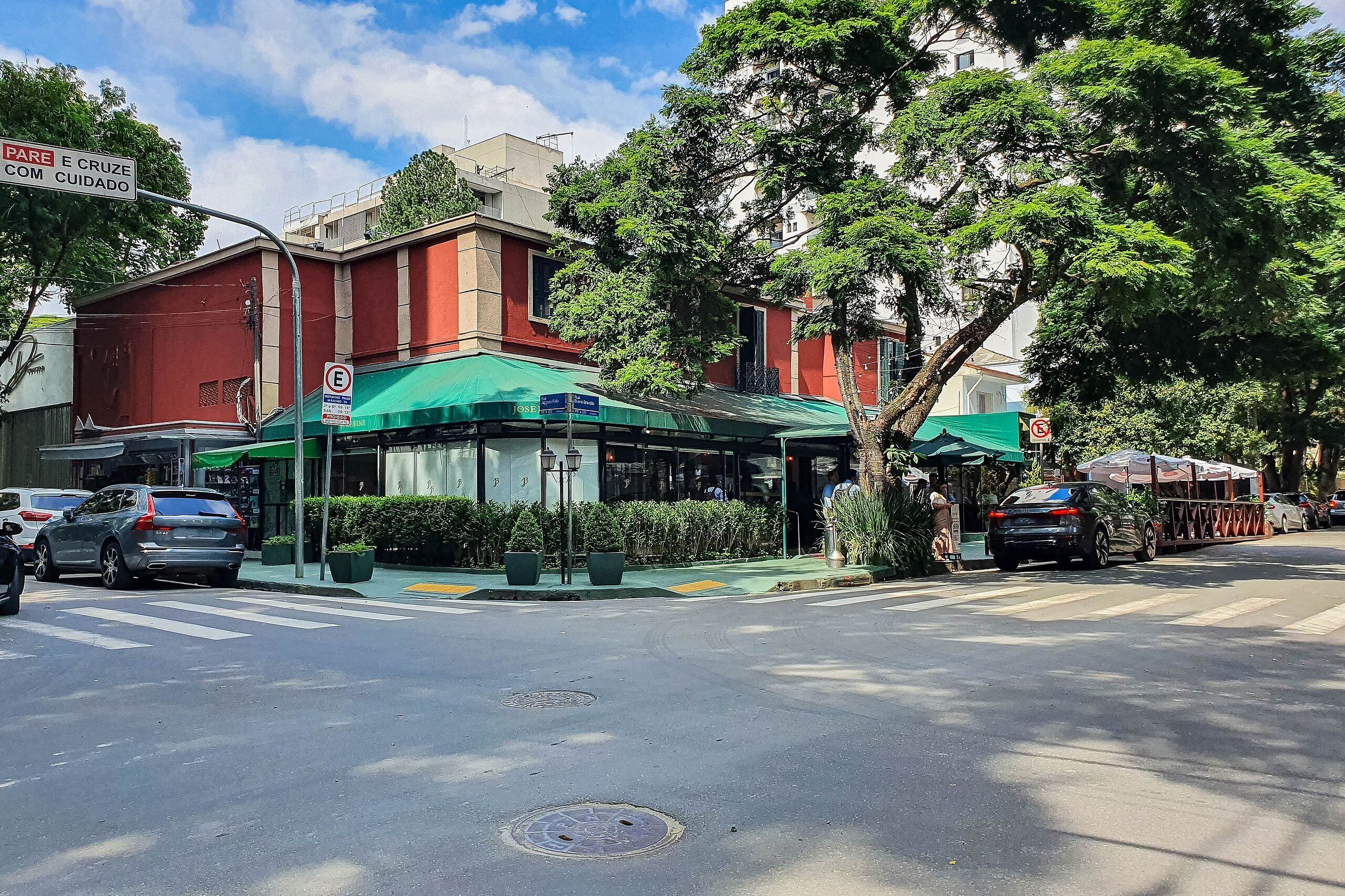 A street view with a green-roofed building, a pedestrian crossing, and parked cars.