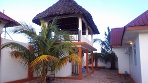 Un patio con una estructura de techo de paja, palmeras y piso de baldosas.