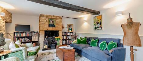 Un salon chaleureux avec une cheminée en pierre, un canapé bleu, des coussins verts, une table basse en bois et un mannequin sur un trépied.