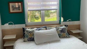 Un dormitorio con una cama, dos mesitas de noche, un ventanal con persianas y un cuadro en la pared.