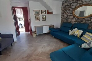 Un salon avec un canapé bleu, un fauteuil gris, un mur en pierre et un miroir.