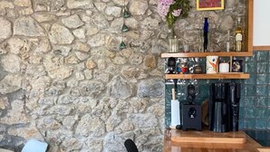 Eine Steinsäule, ein Holztisch, ein schwarzer Stuhl und ein Regal mit diversen Gegenständen.