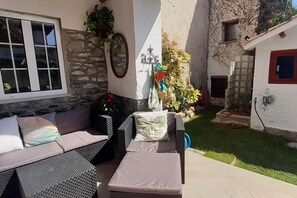 Eine Terrasse mit einer Couch, einem kleinen Tisch und einem Stuhl. Ein Fenster bietet Blick auf den Himmel.