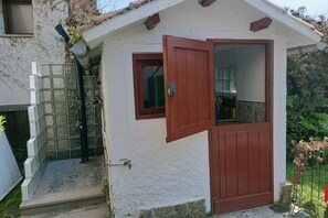 Ein kleines, weißes Gebäude mit roter Tür und Fenster, mit einer gefliesten Eingangspforte und einem kleinen Garten.