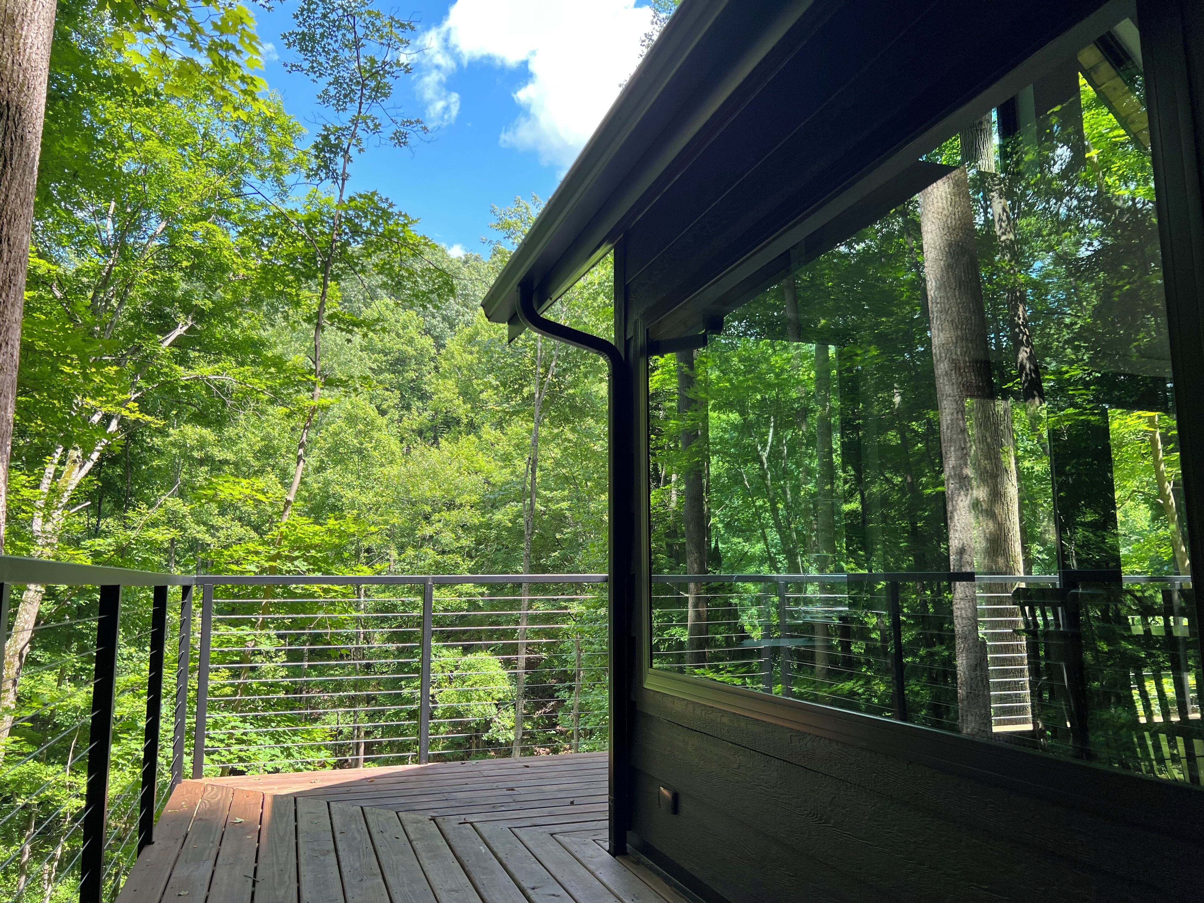 A wooden deck with a metal railing overlooking a forested area.