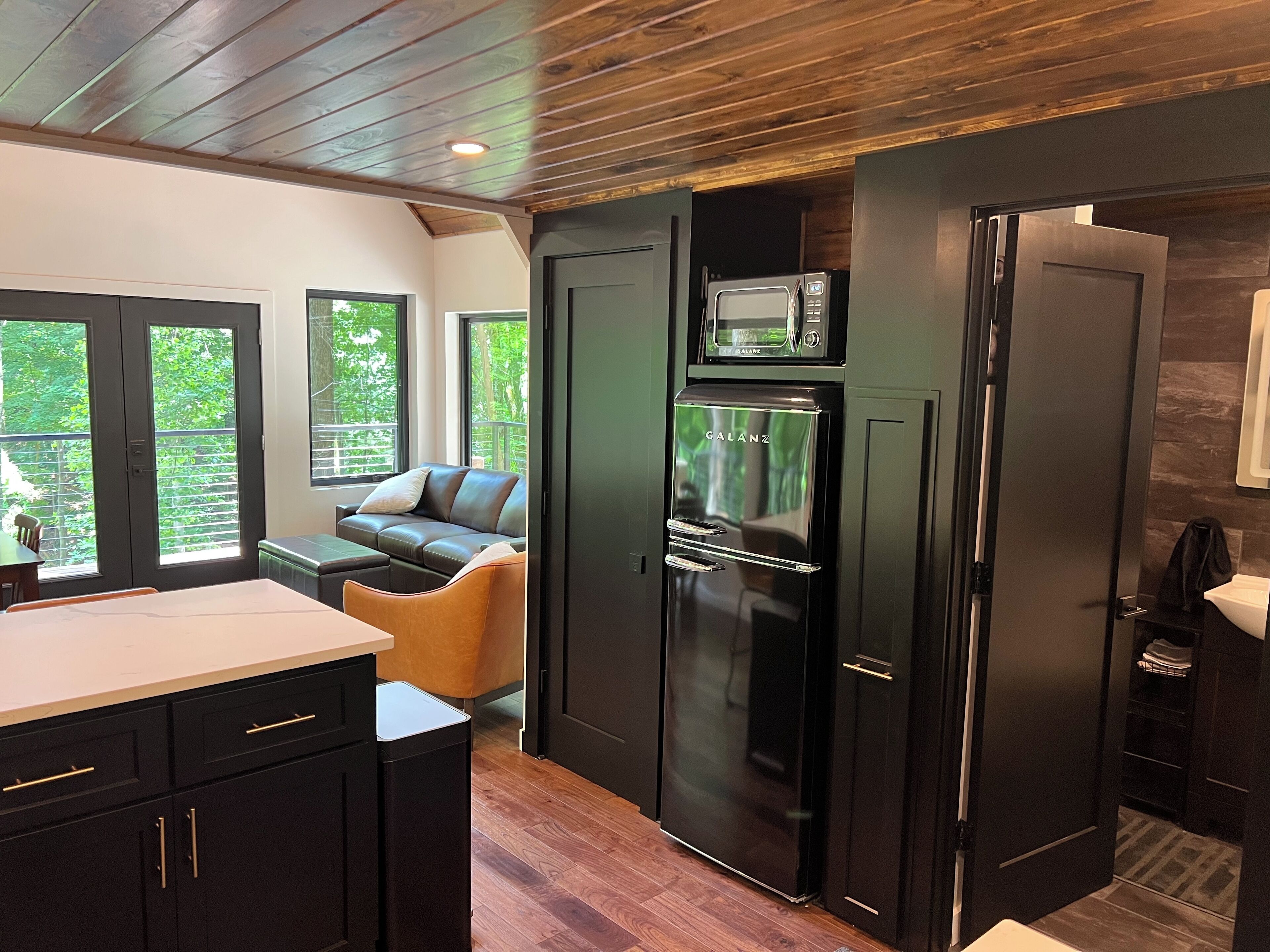 Cocina compacta con microondas integrado, refrigerador y comedor con sofá y mesa.