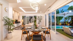A modern dining area with a glass table, wooden chairs, and a central vase of flowers. - Peaceful Retreat-2BR,Canggu (Mengwi)