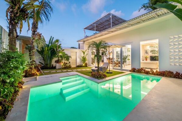 Ein modernes Haus mit Swimmingpool, Sitzgelegenheiten im Freien und üppiger Bepflanzung.