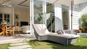 A modern outdoor seating area with a wicker lounge chair, a table with chairs, and a large umbrella. - Peaceful Retreat-2BR,Canggu (Mengwi)