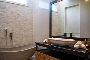 Ein modernes Badezimmer mit freistehender Badewanne, einem großen Spiegel und einem schwarzen Waschtisch mit weißem Becken.