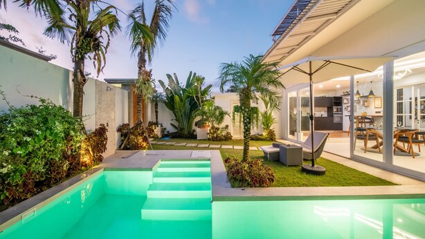 A modern outdoor pool area with steps leading into the water, surrounded by lush greenery and palm trees. - Peaceful Retreat-2BR,Canggu (Mengwi)