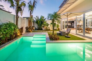 Un espace piscine extérieur moderne, avec des marches menant à l’eau, entouré d’une végétation luxuriante et de palmiers.