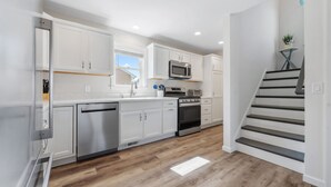 A modern kitchen with white cabinetry, stainless steel appliances, and a wooden floor. - Newly Built Luxury Townhouse in Ortley Beach! (Seaside Heights)