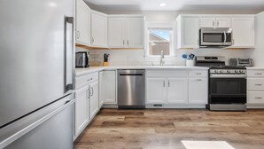 A modern kitchen with white cabinets, stainless steel appliances, and a wooden floor. - Newly Built Luxury Townhouse in Ortley Beach! (Seaside Heights)