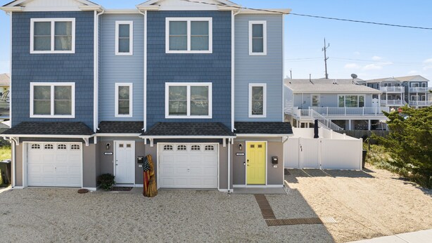 A two-story residential building with a garage, a front door, and a small porch area. - Newly Built Luxury Townhouse in Ortley Beach! (Seaside Heights)