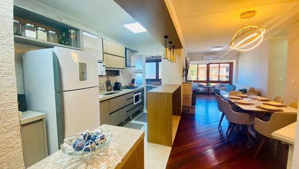 A modern kitchen with a refrigerator, microwave, and stove, leading to a dining area with a wooden table and chairs.