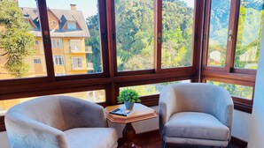 A room with two armchairs, a small table with a plant, and large windows offering a view of a building and trees.