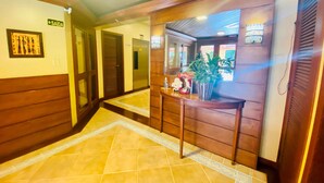 A hotel lobby with a tiled floor, wooden paneling, a reception desk, and a sign indicating the exit.