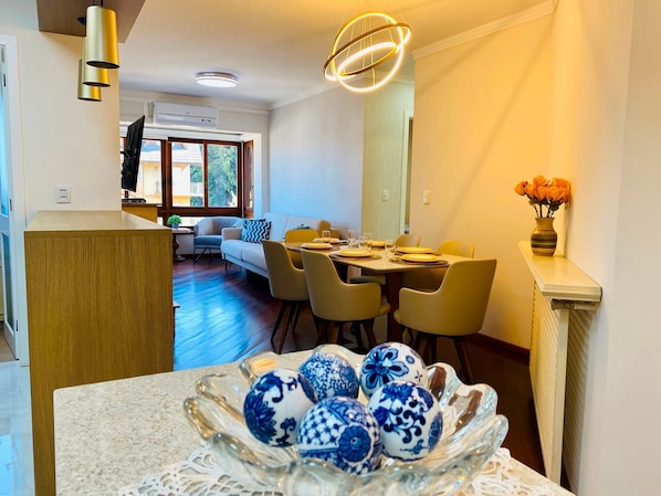 Uma área de refeições com uma mesa posta para quatro pessoas, um sofá e uma tigela decorativa com ovos de cerâmica azul e branco.