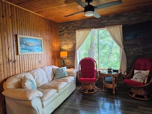 A cozy room with a wooden ceiling, a white leather sofa, two red chairs, a small table, and a window with curtains.
