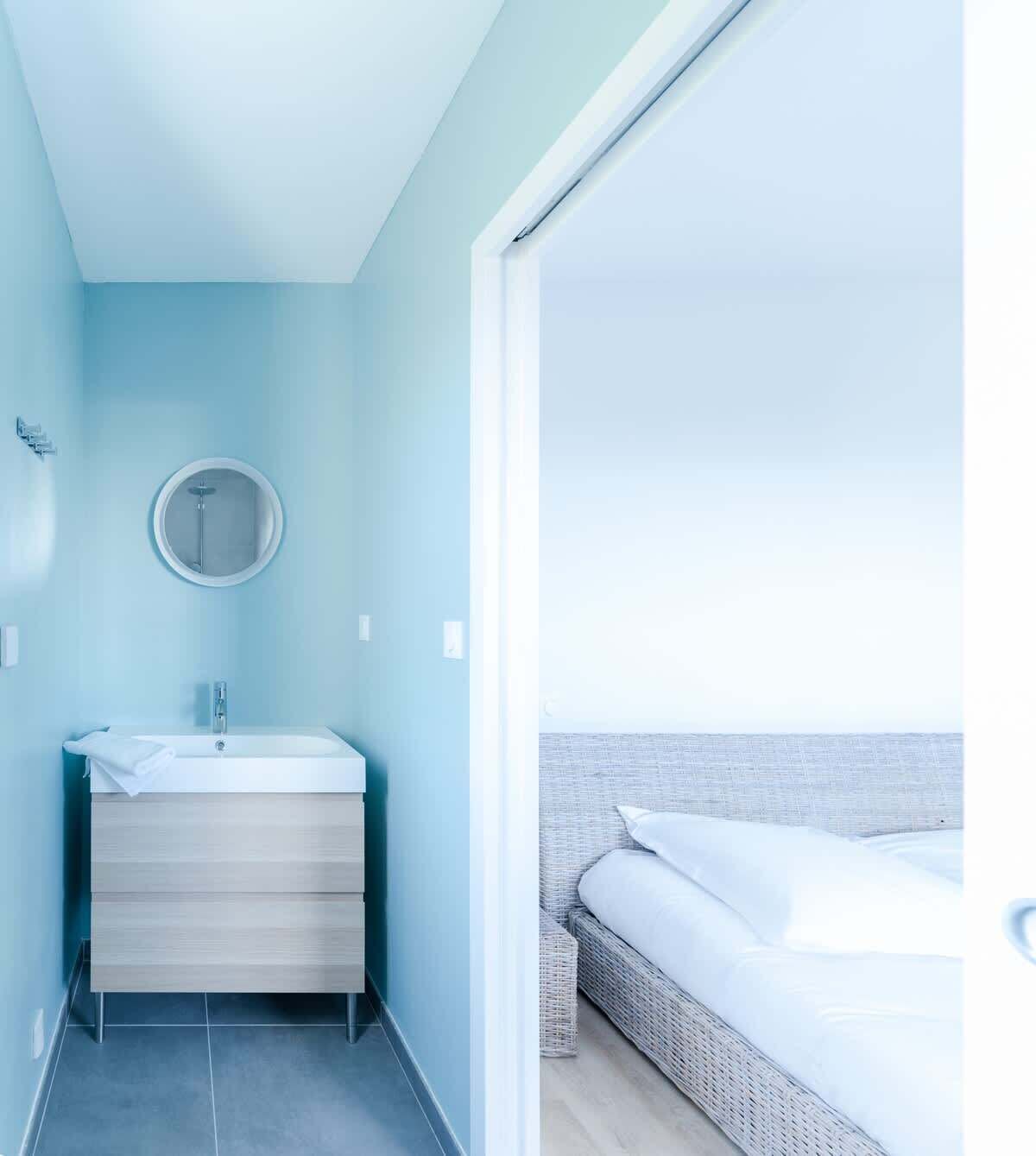 Ein modernes Badezimmer mit einem weißen Waschbecken, einem Spiegel und Meerblick durch ein großes Fenster.
