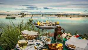 A lakeside dining setup with seafood, wine glasses, and a view of boats on the water.