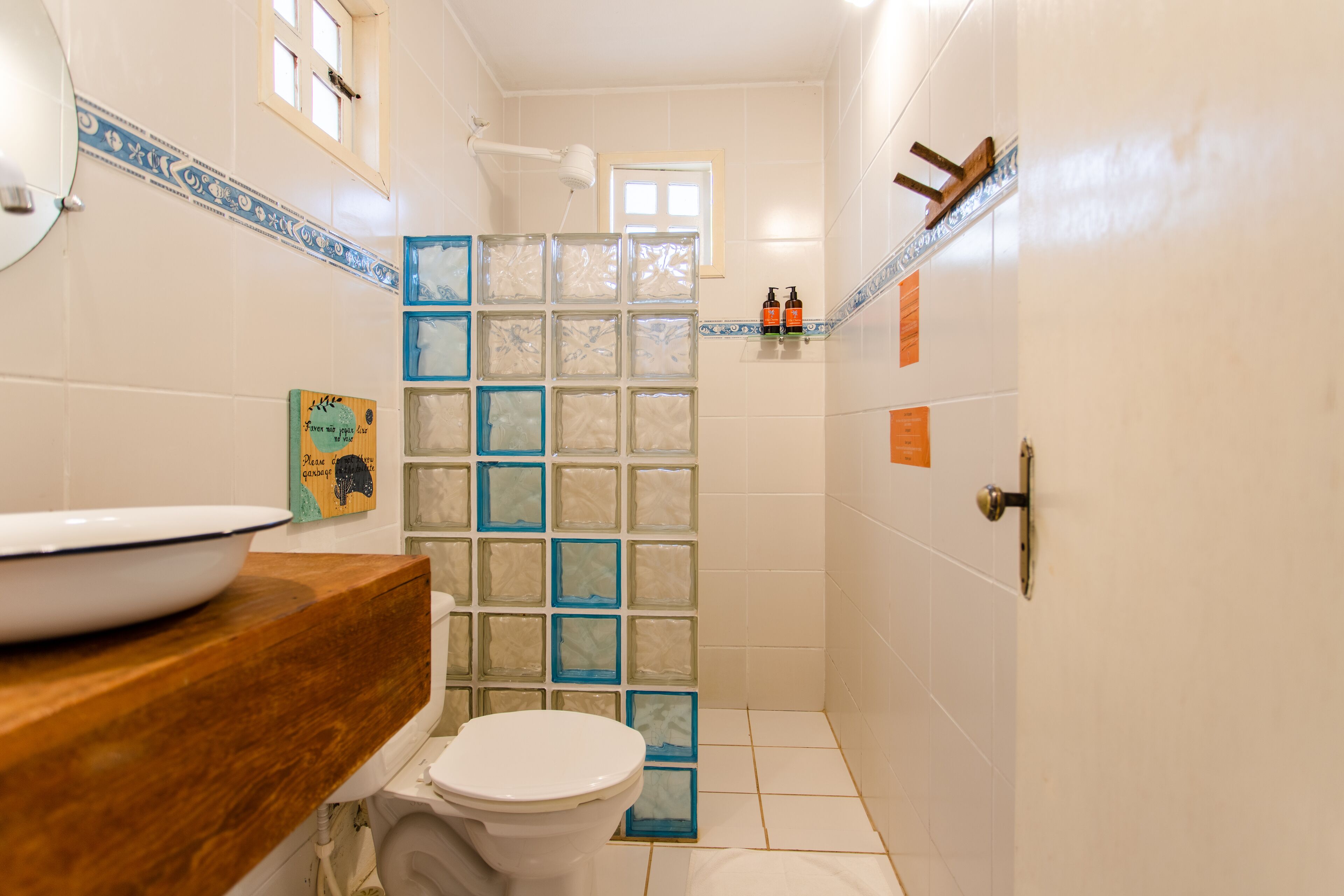 Een badkamer met een houten wastafelmeubel, een wit toilet en een douchecabine van glas, en decoratieve tegels.