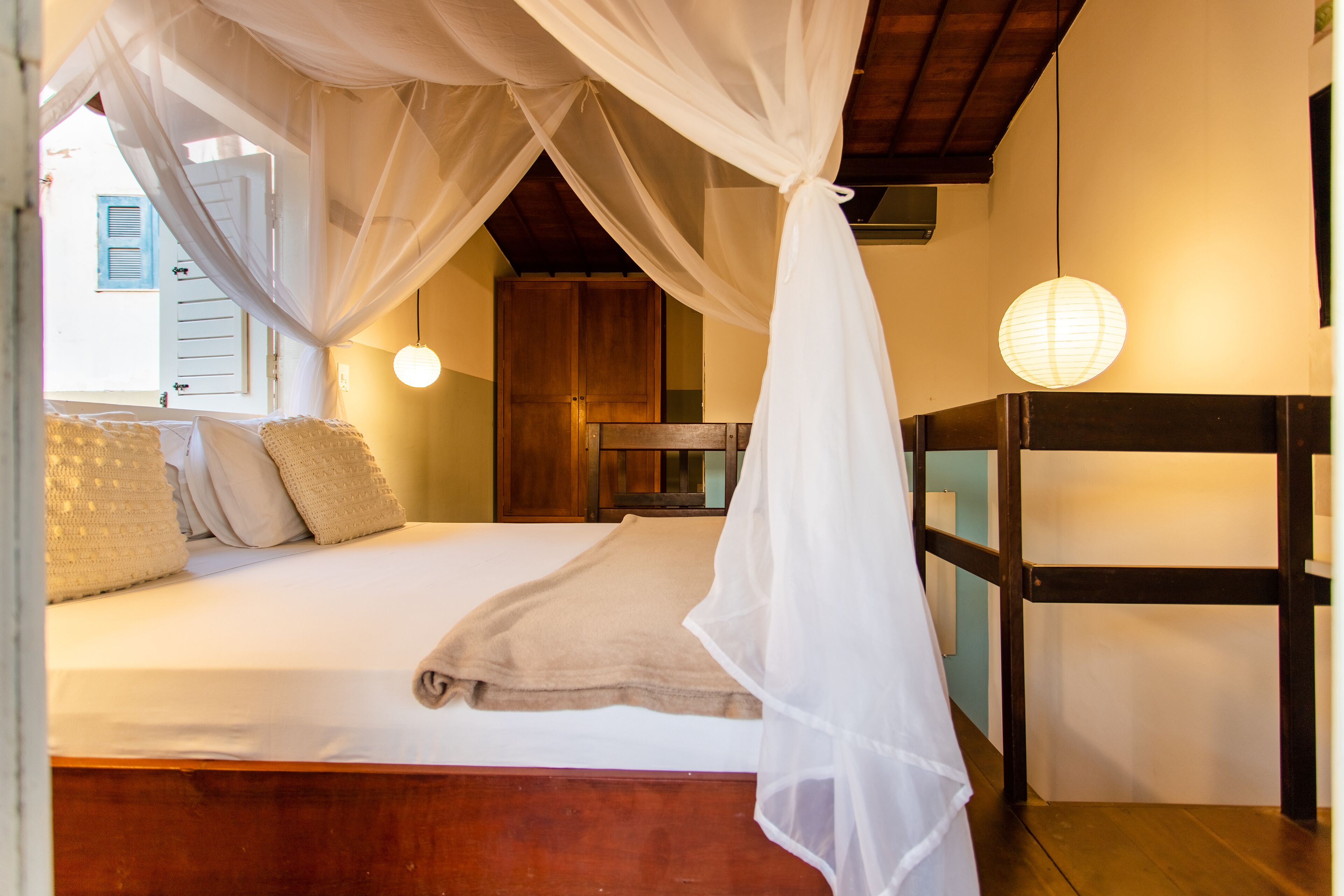 A room with a bed under a canopy, a wooden headboard, a bedside table, and a hanging light fixture.