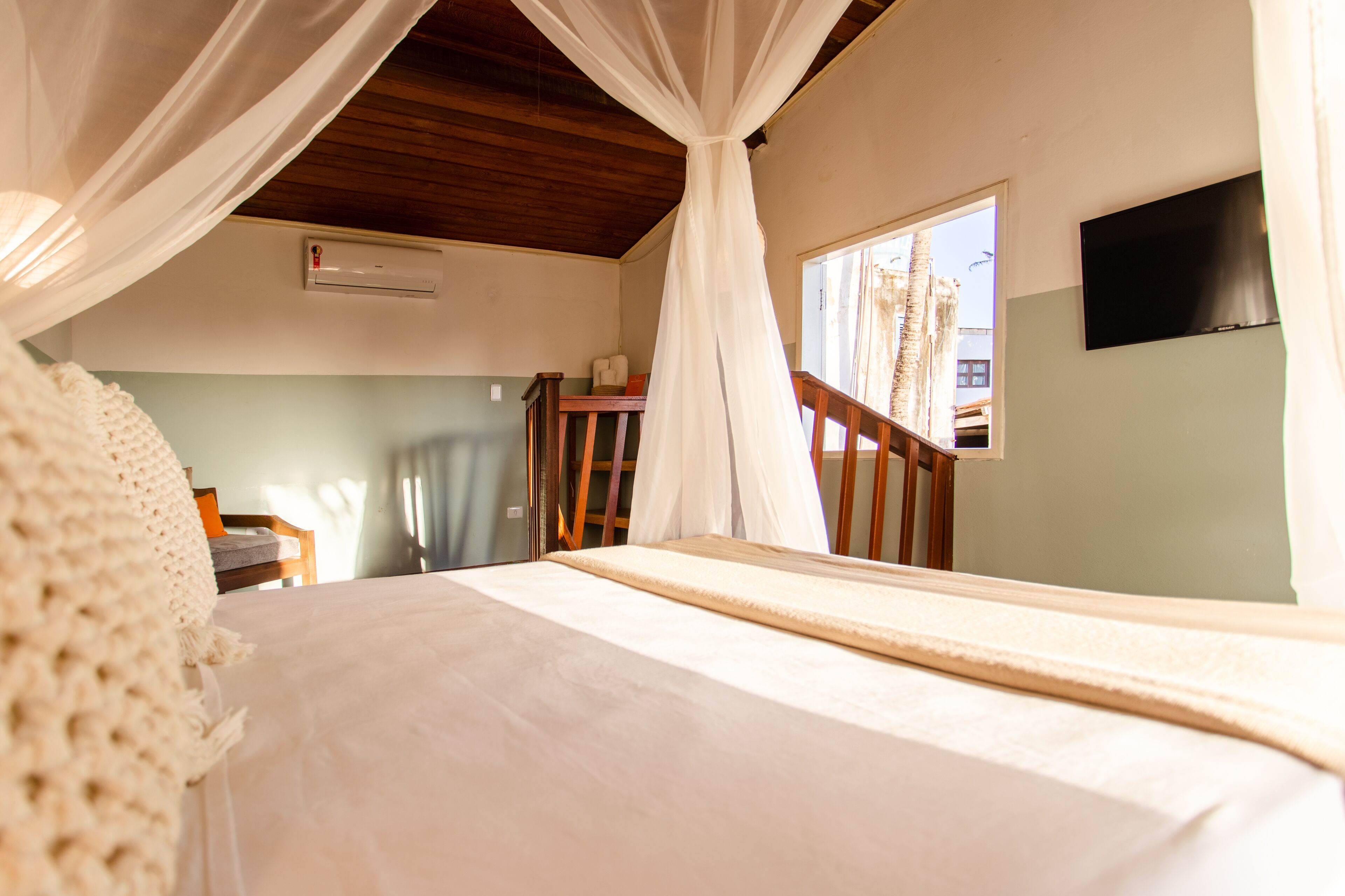 A bedroom with a bed, a wooden ceiling, a window, and a TV on the wall.