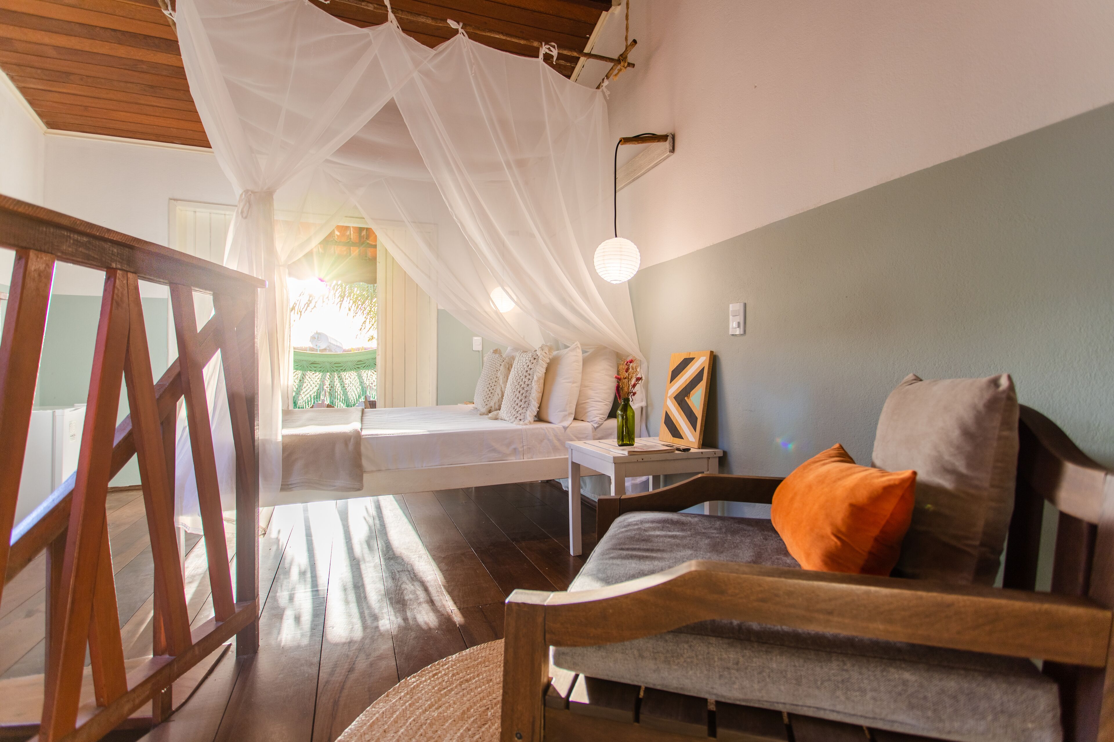 A room with a bed, a wooden bench, a table with a vase, and a hanging light fixture.