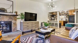 Un soggiorno moderno con camino in pietra, una TV a schermo piatto, un'area pranzo con sgabelli da bar e una cucina con mobili in legno.