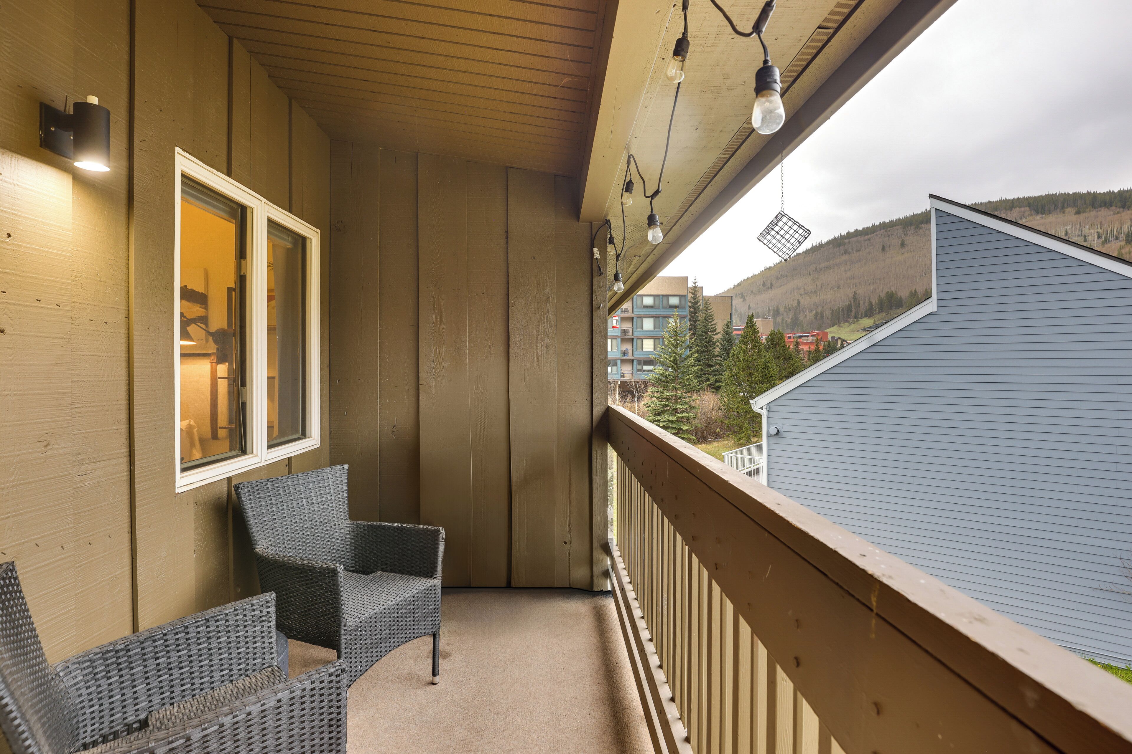 A balcony with wicker furniture, a wooden ceiling, and a view of a building and trees.