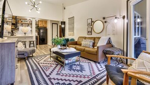 Un soggiorno moderno con divano, tavolino e tappeto decorato. Presente un angolo cottura con mobili in legno e frigorifero.