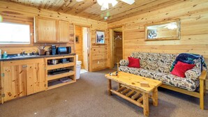 Interior d'una cabana de fusta amb una cuineta, un sofà i un ventilador de sostre.
