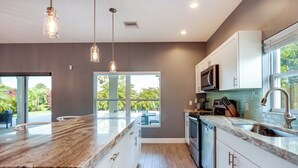 A modern kitchen with a large island, white cabinets, and a view to the outdoors. - Florida Gem: Saltwater Pool By Beaches & Kayaking! (Jensen Beach)