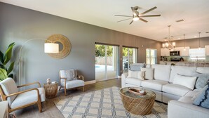 A spacious living room with a large sofa, two armchairs, a coffee table, and a floor lamp. There is a sliding glass door leading to a patio area. - Florida Gem: Saltwater Pool By Beaches & Kayaking! (Jensen Beach)