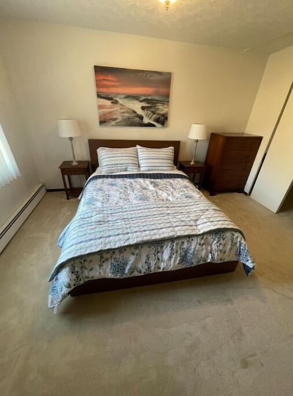 A bedroom with a bed, two bedside tables, a nightstand, a dresser, and a painting on the wall. - Home in the heart of Eagle River (Anchorage)