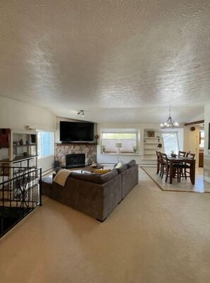 A spacious living room with a fireplace, a large TV, a dining area with a table and chairs, and a staircase leading to another level. - Home in the heart of Eagle River (Anchorage)