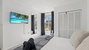 A bedroom with a bed, a TV on the wall, a window with curtains, and a closet. - My Disney Home (Kissimmee)