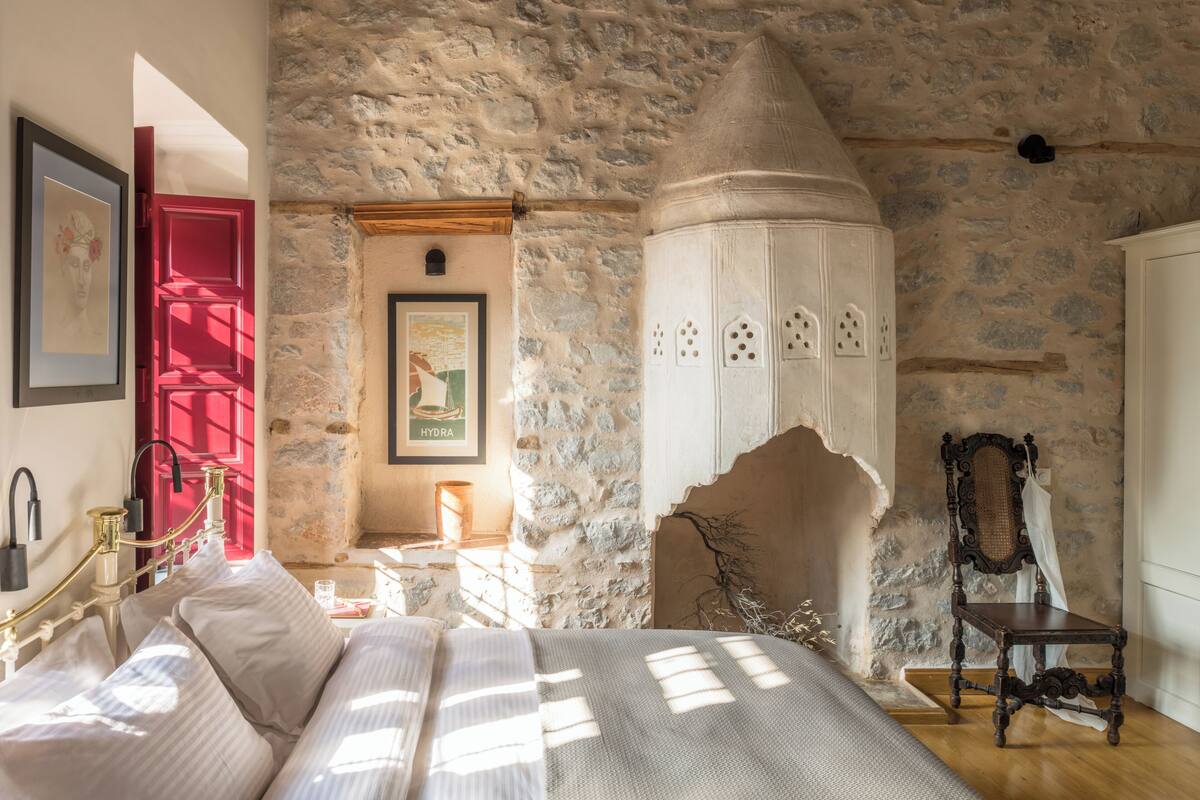 Un dormitorio con pared de piedra, una cama con ropa blanca, una puerta roja y un armario blanco.