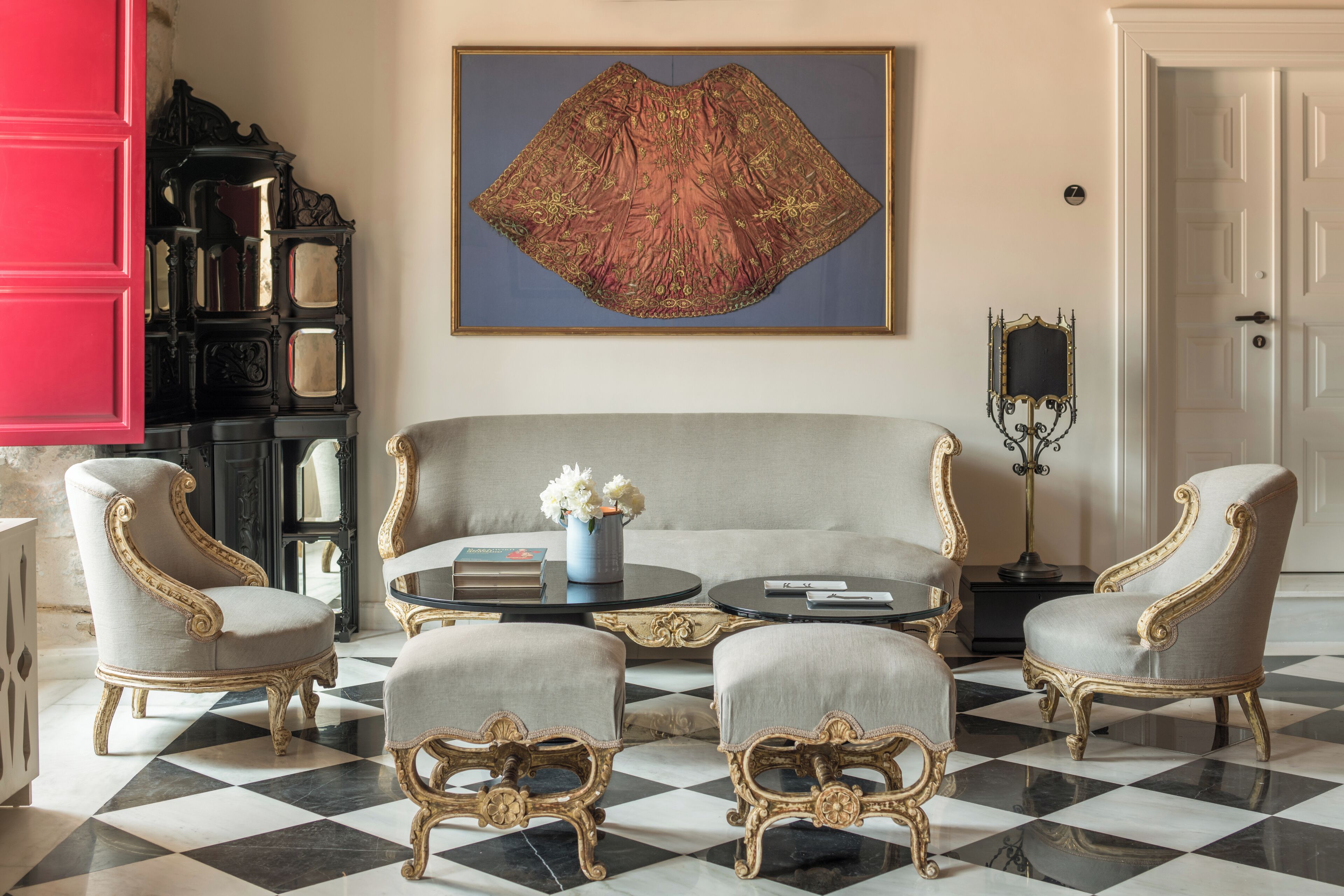 Una habitación con suelo a cuadros, un sofá, dos sillones, una mesa de centro, una estantería y un cuadro.