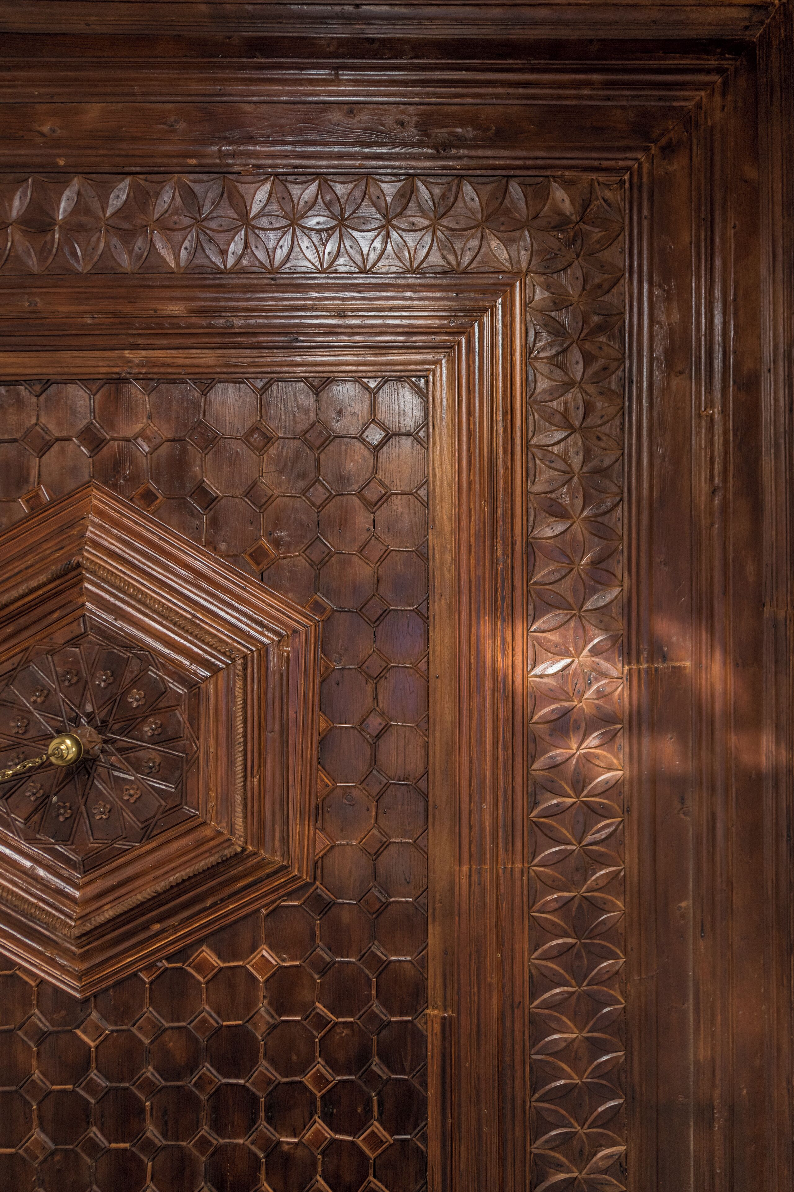 Una puerta de madera con intrincados diseños geométricos y un aldabón de bronce central.
