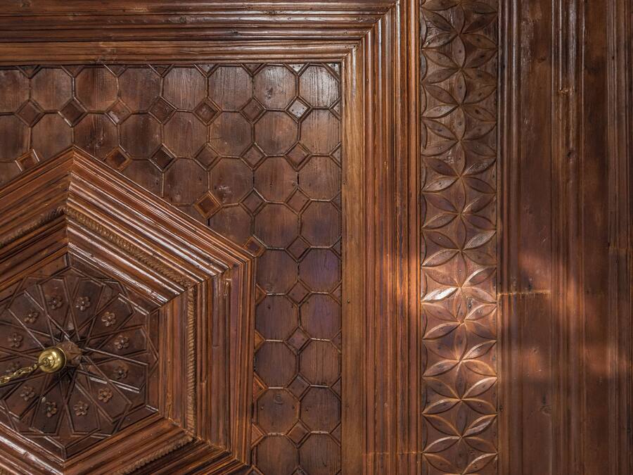 Una puerta de madera con intrincados diseños geométricos y un aldabón de bronce central.