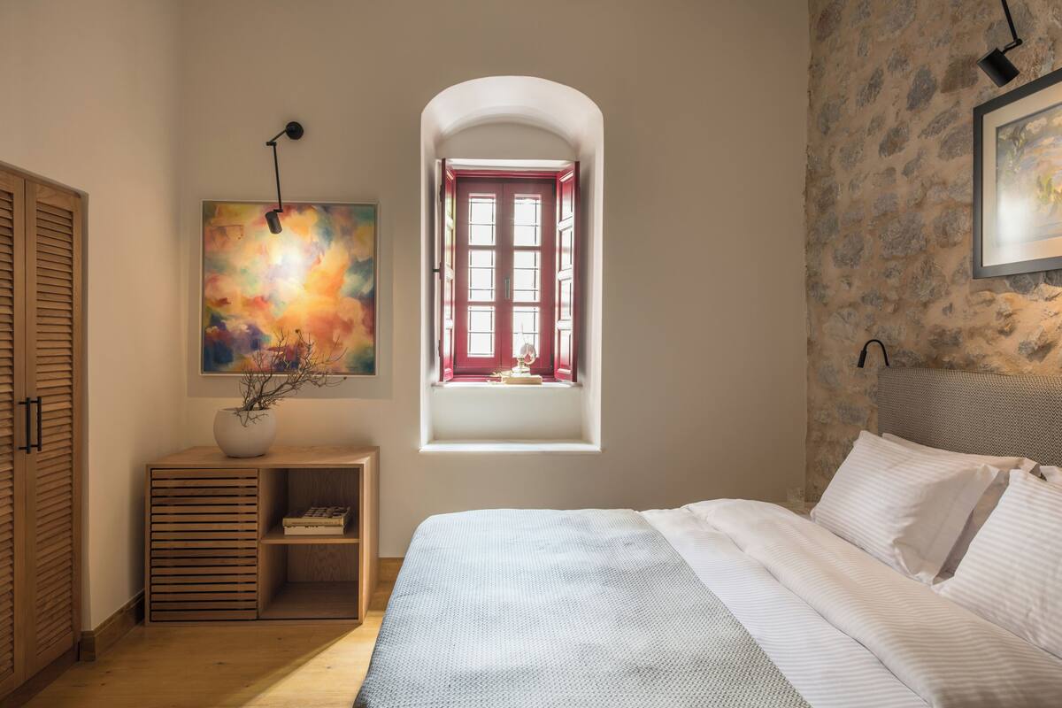 Un dormitorio con cama, ventana, cuadro y lámpara.