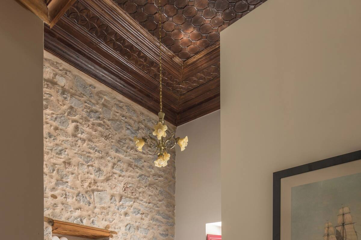 Un dormitorio con pared de piedra, cama con ropa blanca, cabecero de madera, lámpara colgante y un cuadro en la pared.