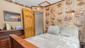 A bedroom with a wooden bed frame, a white comforter, a wooden dresser, and a door leading to another room. - Boulder Pines (Big Bear Lake)