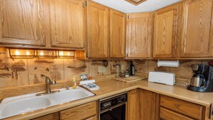 A kitchen with wooden cabinets, a sink, a dishwasher, a toaster, and a coffee maker. - Boulder Pines (Big Bear Lake)