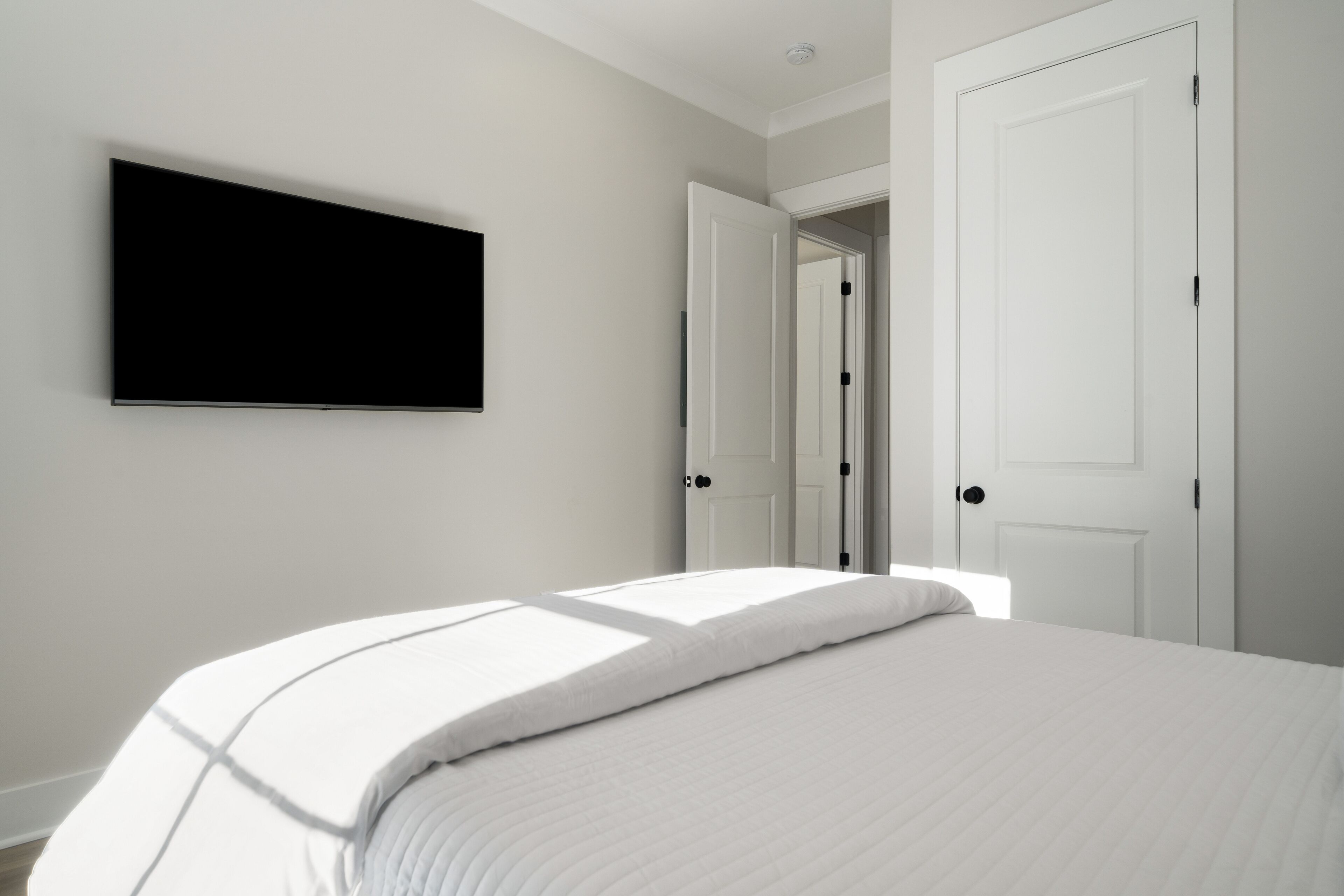 A bedroom with a bed, a flat-screen TV mounted on the wall, and two doors.