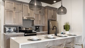 A modern kitchen with wooden cabinets, stainless steel appliances, a large island with bar stools, and pendant lighting. - 2 Bedroom, Main Level (Helena)