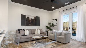A modern living room with a sofa, armchairs, a coffee table, and a dining area with clear chairs. - 2 Bedroom, Main Level (Helena)